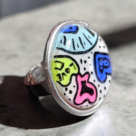 La bague Popsi est un accessoire unique en argile polymère. Ce bijou multicolore est phosphorescent à la lumière bleue, ajoutant une touche de fantaisie à votre look. Son anneau en acier inoxydable est réglable pour un ajustement parfait sur tous les doigts. Son diamètre de 2,6 cm