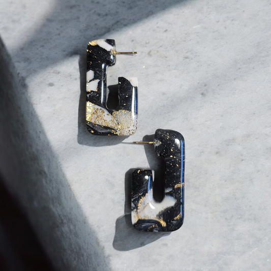 Ces boucles d'oreille en argile polymère noires et blanches embellies de feuilles d'or sont un choix élégant. Les tiges plaquées or 18 carats assurent une qualité supérieure. Avec une longueur totale de 4,4cm